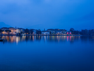 Naklejka premium Lugano city buildings illuminated at night on lake Lugano in Switzerland