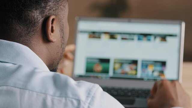 Over shoulder view of male unrecognizable african man american young web designer programmer freelancer look at laptop screen develop online project scroll internet website page chose modern interface