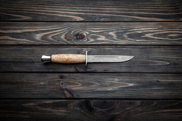 Hunting knife with wooden handle. Damascus steel blade. Vintage wooden background from planks.