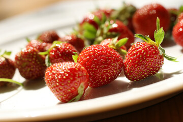 Fresh strawberries on the white plate on wooden table. Fresh nice strawberries. Heap of Red strewberry on plate close up. Juice strawberry. Strawberry on fruit farm.