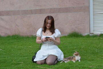girl in white dress playing with street cat on green grass