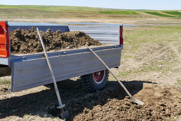 a peasant filling his tractor trailer with soil, a peasant filling soil with a shovel