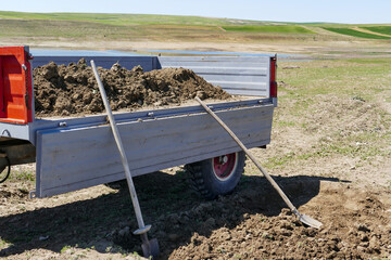 a peasant filling his tractor trailer with soil, a peasant filling soil with a shovel