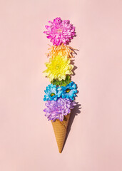 Colorful flowers in ice cream cone on light pastel pink background. Creative food concept. Minimalistic nature composition. Sunny summer day idea.