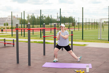 An obese woman does sports on a public sports ground. Outdoor training. Weight loss, positive body,...