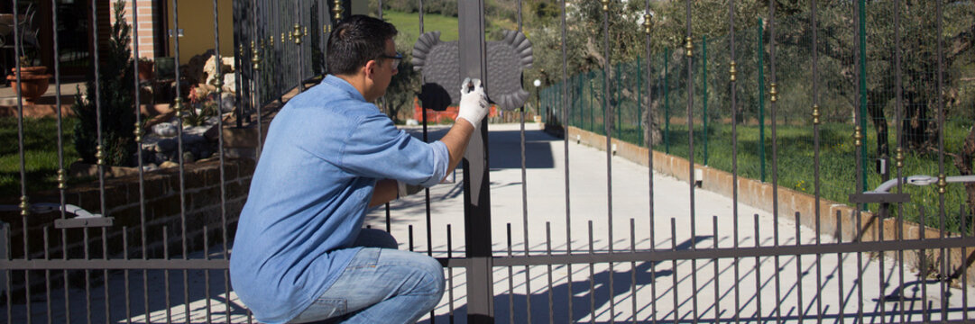 Picture of a handyman painting the driveway gate of the house. Horizontal banner 