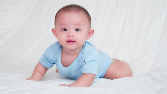 Happy family, Cute Asian newborn baby wear blue shirt lying, crawling play on bed looking at camera with laugh smile happy face. Innocent little new infant adorable. Parenthood and Mother Day concept.