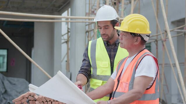 Professional male civil engineer or Architect, inspector with contractor, foreman or worker. While look at blueprint plan inspect discuss meeting building project and pointing on construction site.