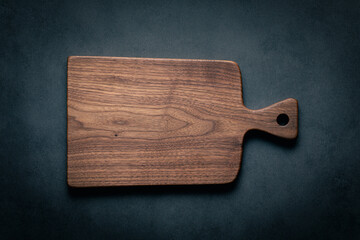 A handcrafted black walnut wood chopping board sits on a dark-toned tabletop. walnut wood board. - obrazy, fototapety, plakaty