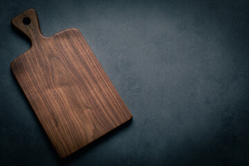 A handcrafted black walnut wood chopping board sits on a dark-toned tabletop. walnut wood board.