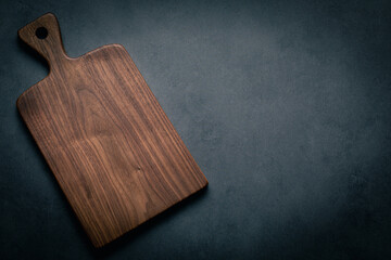A handcrafted black walnut wood chopping board sits on a dark-toned tabletop. walnut wood board.