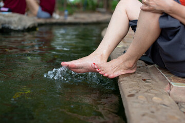 A happy asian young woman relaxing in a hot spring and using her foot to bail out the water.