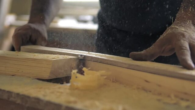 Slow motion the woodworking milling cutter removes chamfers from the edge of a board with a large amount of sawdust. Carpenter in the workshop, makes furniture parts in natural light. Carpentry tools