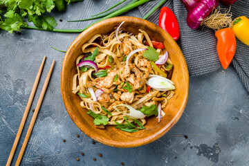 Udon noodles with chicken and vegetables on wooden bowl on grey table top view
