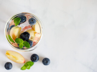 Blueberry and peach infused water, cocktail, lemonade or tea in double glass. Summer iced cold drink with blueberry, ice, peach and mint on grey marble background, copy space, top view flat lay