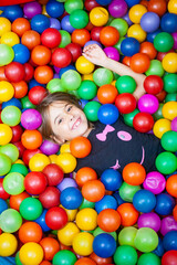 Kind liegt in einem Ballpool, bunte Bälle und ein Mädchen