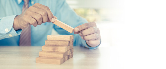 Hand placing wooden block tower stack in pyramid stair step with caution to prevent collapse or...