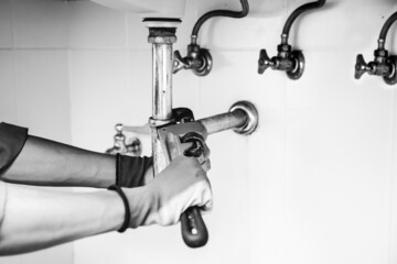 Technician plumber using a wrench to repair a water pipe under the sink. Concept of maintenance,...