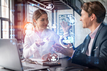 Businessman and businesswoman in formal wear working together looking for new employees to hire for international business consulting. HR, social media icons over modern panoramic office background
