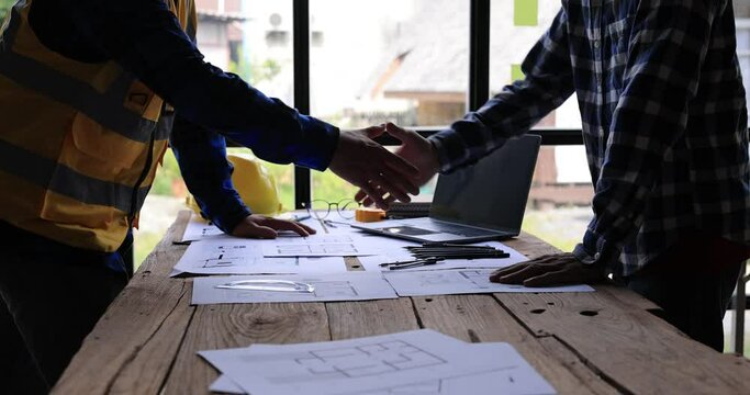 Two Civil Engineer or Architect holding helmet and handshaking after mega project done. handshake engineer sketching a construction project concept.4K side view.