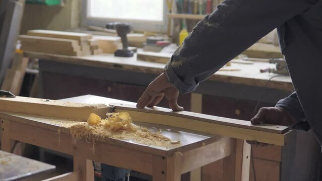 Slow motion the woodworking milling cutter removes chamfers from the edge of a board with a large amount of sawdust. Carpenter in the workshop, makes furniture parts in natural light. Carpentry tools