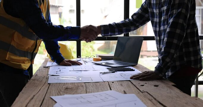 Two Civil Engineer or Architect holding helmet and handshaking after mega project done. handshake engineer sketching a construction project concept.4K side view.
