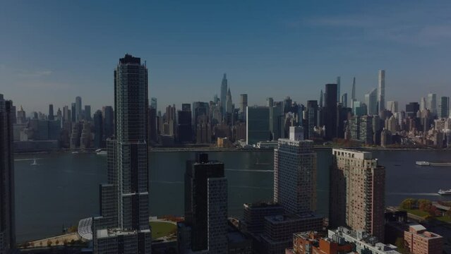 Forwards fly around high rise apartment buildings. Revealing panoramic view of river and tall downtown skyscrapers. Manhattan, New York City, USA