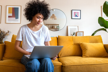 Young African american woman sitting on the couch using laptop working at home. Copy space.