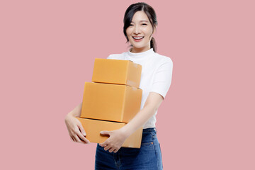 Happy Asian girl holding package parcel boxs isolated on pink screen background. Delivery courier...