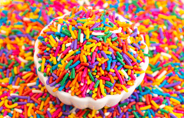 Fototapeta na wymiar A Bowl of Rainbow Sprinkles on a Table of Sprinkles