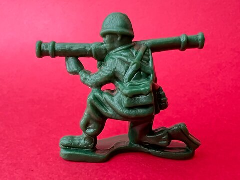 敵へ向かって銃を構える兵士の人形（赤背景）、戦争イメージ