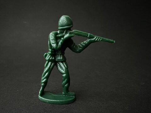 敵へ向かって銃を構える兵士の人形（黒背景）、戦争イメージ