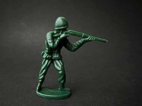 敵へ向かって銃を構える兵士の人形（黒背景）、戦争イメージ