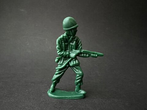 敵へ向かって銃を構える兵士の人形（黒背景）、戦争イメージ