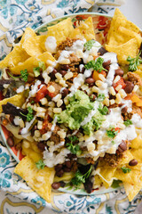 A plate of delicious plate of nachos. On the nachos is corn, avocado, salsa, tomatoes, chips, black beans, cheese and sour cream