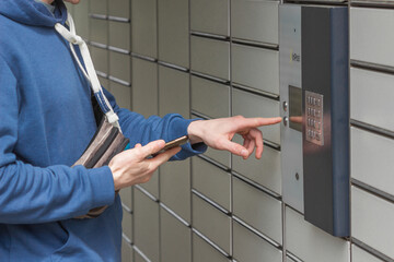Man with smartphone entering code to open shopping locker in inPost delivery service. People and gadgets concept.