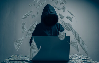 The hacker was wearing a black hoodie. Stealing huge financial data on computers with binary code digital interface and lots of falling dollars and lying on the table.Hacking and malware concept.