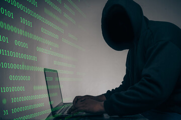 The hacker was wearing a black hoodie. Stealing huge financial data on computers with binary code digital interface and lots of falling dollars and lying on the table.Hacking and malware concept.