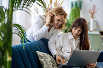 Two girls in shirts are discussing something while looking at the phone and a magazine in the apartment