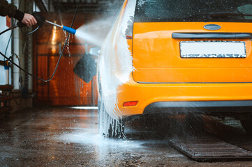 Washing a yellow car at a contactless self-service car wash. Washing a sedan car with foam and...