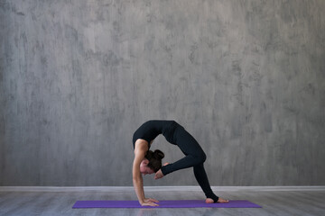 Athletic young woman practice yoga down, face down isolated on gray wall background in black sportswear. Concept healthy lifestyle and natural balance between body and mental development. Full lengths