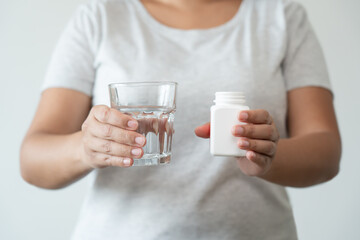 Asian woman close up ready to take supplement pill holding a glass of water. Sick person need medicine and water for good health.