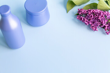 Two purple jars with cosmetic products and creams with fresh, blooming and fragrant lilac flowers and free space for advertising.