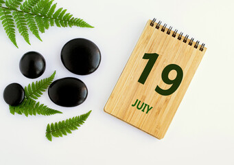 July 19. 19th day of the month, calendar date. Notepad, black SPA stones, green leaves. Summer month, day of the year concep