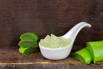 Aloe vera gel in white bowl with fresh aloe vera on rustic wooden background.