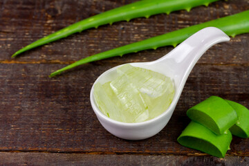 Aloe vera gel in white bowl with fresh aloe vera on rustic wooden background.