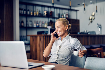A happy businesswoman sits in a working friendly cafe and having an important call. 