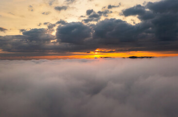 aerial view over the clouds during sunrise. Golden hour and amazing sunrays, beautiful cloudscape. Picturesque of white fluffy clouds moving softly on cloudy, misty weather.