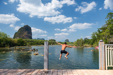 Fototapeta na wymiar Rear of happy energic boy jump to river with blue sky and Limestone karst mountain at Klong Rood, Krabi, Thailand. Holiday and summer vacation to kayak and swim in Siam.