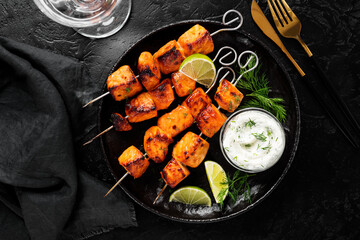 Grilled salmon skewers with  cheese sauce and greens. Black background. Top view